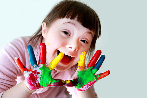 تصویری از یک کودک مبتلا به سندروم داون با دست های رنگی
