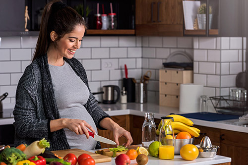 تصویری از یک خانم باردار در آشپزخانه که دارد برای خود سالاد میوه درست میکند
