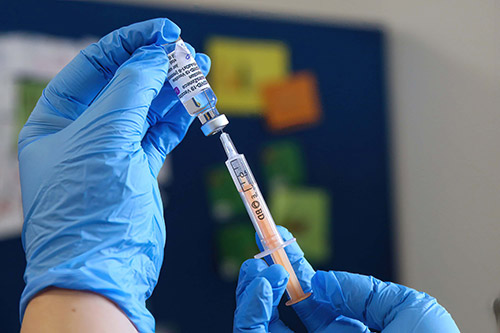 تصویری از دست یک دکتر که دارد با یک سرنگ از ویال واکسن کرون آمپول خود را پر میکند