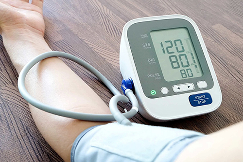 تصویری از یک دست یک مرد در حال گرفتن فشار خون خود با دستگاه فشار سنج دیجیتال